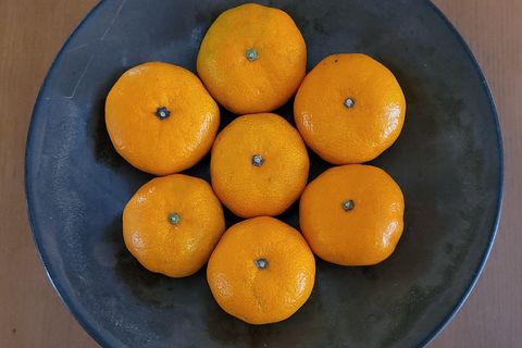 Seven mandarins arranged in a dark ceramic bowl on a wooden table